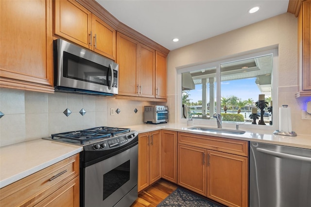 kitchen with a sink, light countertops, appliances with stainless steel finishes, brown cabinets, and backsplash