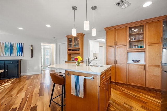 kitchen featuring light wood-style floors, brown cabinetry, visible vents, light countertops, and a sink