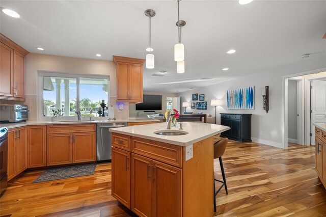 kitchen with open floor plan, light countertops, light wood-style floors, stainless steel dishwasher, and a sink
