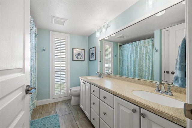 full bath featuring toilet, double vanity, a sink, and visible vents