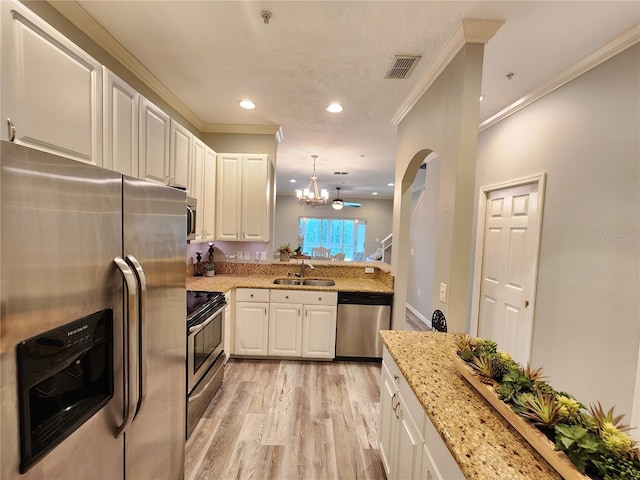 kitchen with a sink, ornamental molding, appliances with stainless steel finishes, light wood finished floors, and a notable chandelier