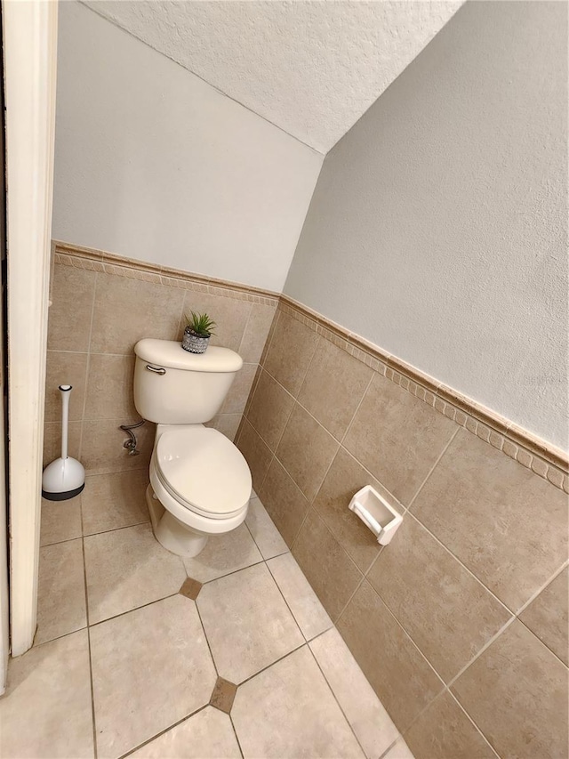 bathroom with a textured ceiling, tile walls, a wainscoted wall, toilet, and tile patterned flooring