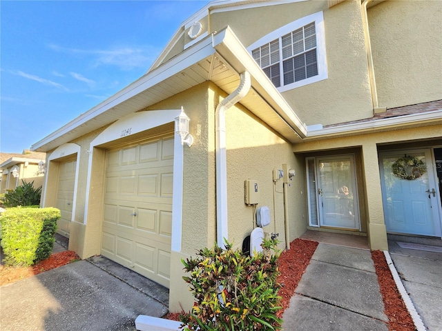 entrance to property with driveway, a garage, and stucco siding