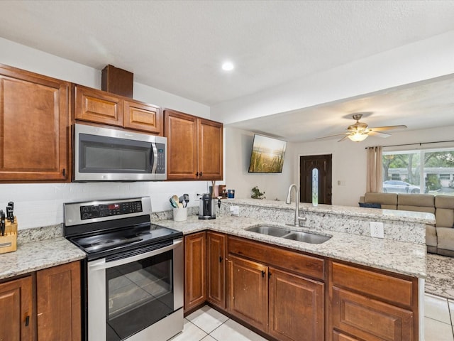 232 Emerald Ln, Largo, FL 33771 - kitchen featuring appliances with stainless steel finishes, a peninsula, light tile patterned flooring, light stone countertops, and open floor plan