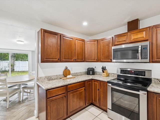 232 Emerald Ln, Largo, FL 33771 - kitchen with stainless steel appliances, light stone counters, and brown cabinetry