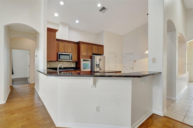 kitchen featuring appliances with stainless steel finishes, light wood finished floors, a breakfast bar area, a peninsula, and visible vents