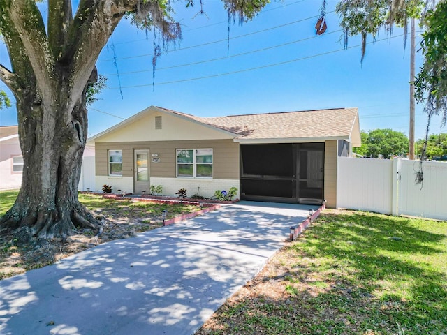 ranch-style house with roof with shingles, a front yard, a sunroom, brick siding, and fence