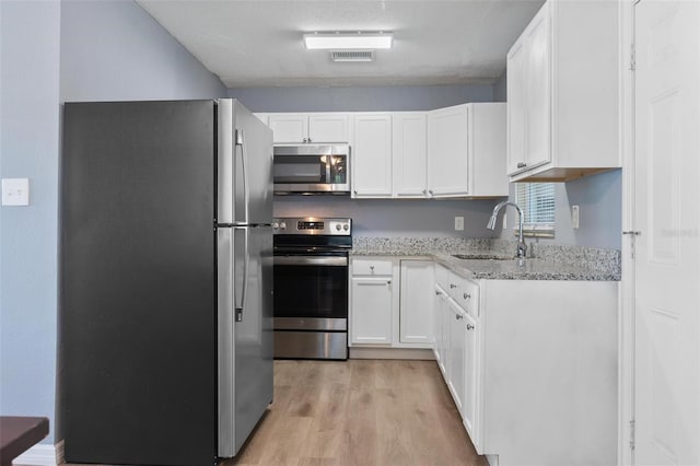 kitchen featuring light wood-type flooring, light stone counters, white cabinets, appliances with stainless steel finishes, and a sink