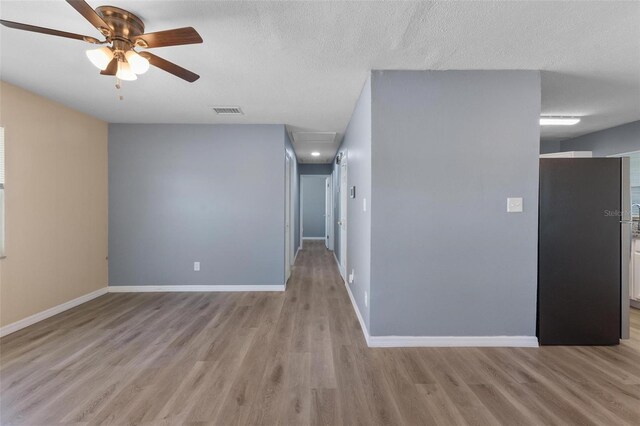 unfurnished room featuring baseboards, light wood-style flooring, attic access, a ceiling fan, and visible vents