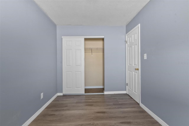 unfurnished bedroom with a textured ceiling, wood finished floors, baseboards, and a closet
