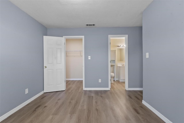 unfurnished bedroom with visible vents, a spacious closet, a closet, and wood finished floors