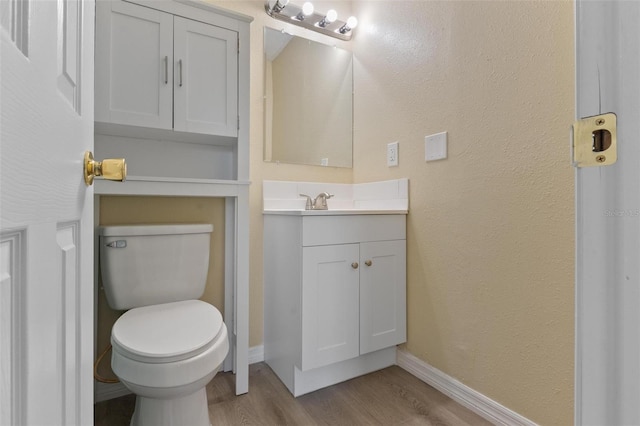 half bathroom with vanity, toilet, wood finished floors, a textured wall, and baseboards