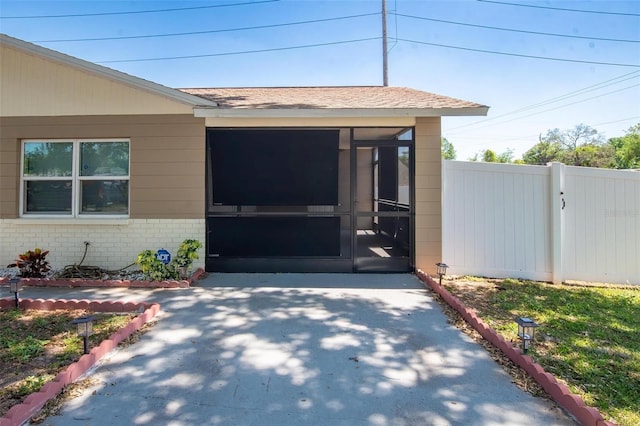 doorway to property featuring roof with shingles, brick siding, and fence