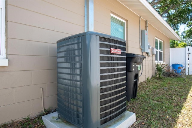 exterior details with cooling unit, concrete block siding, and fence