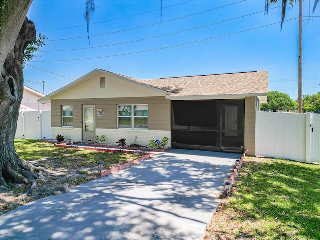 ranch-style home with a sunroom, fence, brick siding, a front lawn, and roof with shingles