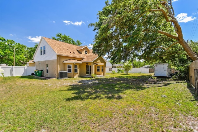 rear view of property featuring an outbuilding, cooling unit, a yard, a fenced backyard, and a storage unit