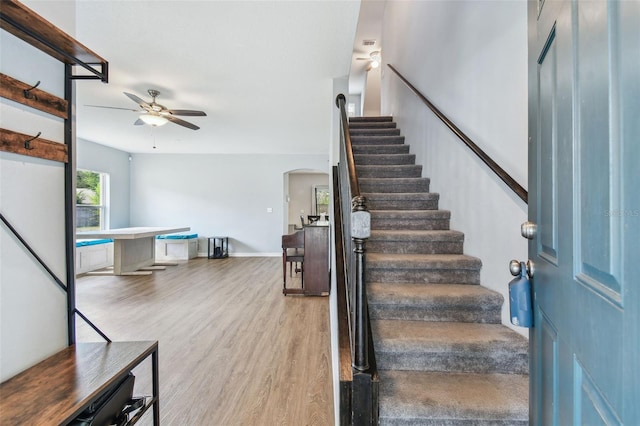 stairs featuring arched walkways, wood finished floors, baseboards, and a ceiling fan