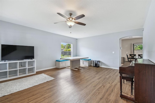 interior space with arched walkways, wood finished floors, ceiling fan, and a healthy amount of sunlight