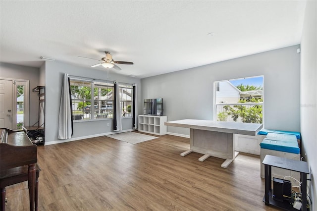 home office with a textured ceiling, a ceiling fan, visible vents, wood finished floors, and baseboards