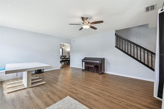 unfurnished living room featuring baseboards, visible vents, ceiling fan, arched walkways, and wood finished floors