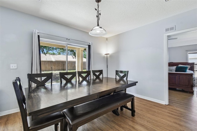 dining area featuring visible vents, a textured ceiling, baseboards, and wood finished floors