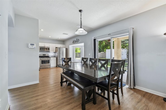 dining space with baseboards, a textured ceiling, and wood finished floors