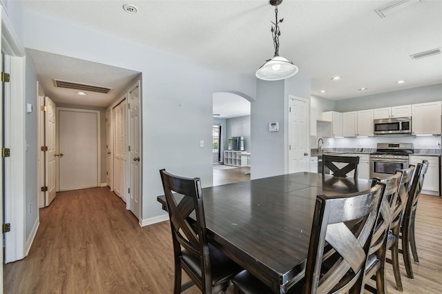 dining room with visible vents, baseboards, arched walkways, and light wood-style floors