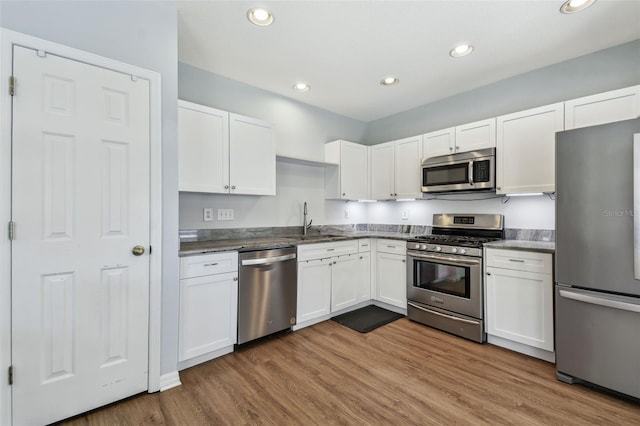 kitchen with stainless steel appliances, white cabinetry, a sink, and wood finished floors