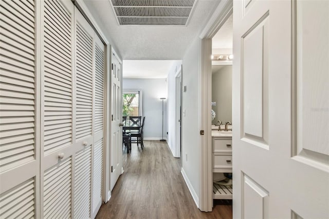 hall featuring visible vents, baseboards, and wood finished floors
