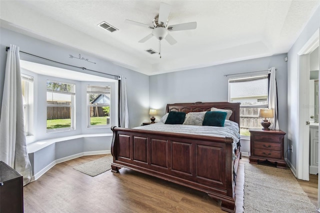 bedroom featuring a raised ceiling, visible vents, baseboards, and wood finished floors