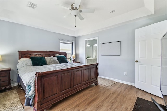 bedroom with a raised ceiling, light wood-style floors, baseboards, and visible vents