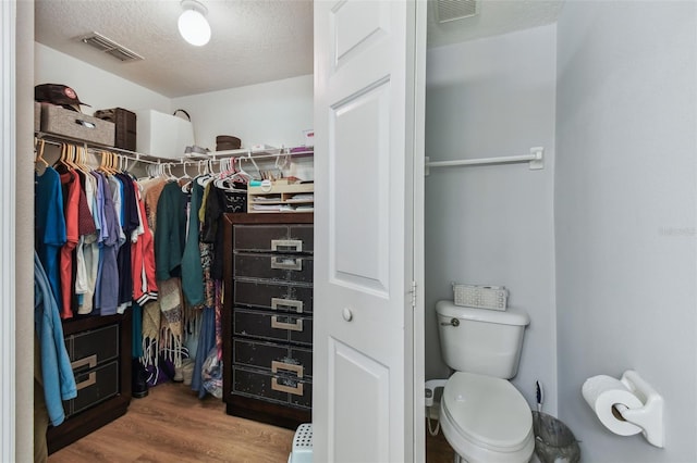 bathroom with visible vents, toilet, a textured ceiling, a walk in closet, and wood finished floors