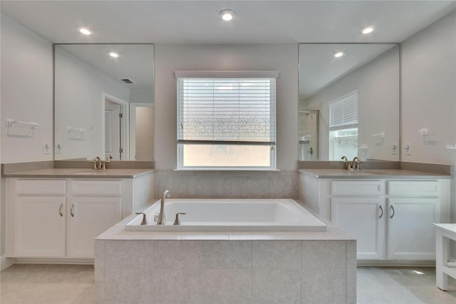 bathroom with a stall shower, a garden tub, two vanities, and a sink