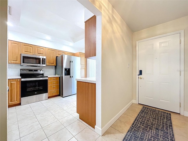 kitchen featuring light tile patterned floors, baseboards, light countertops, stainless steel appliances, and decorative backsplash