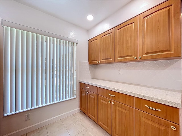 kitchen with light stone countertops, tasteful backsplash, brown cabinetry, and light tile patterned floors