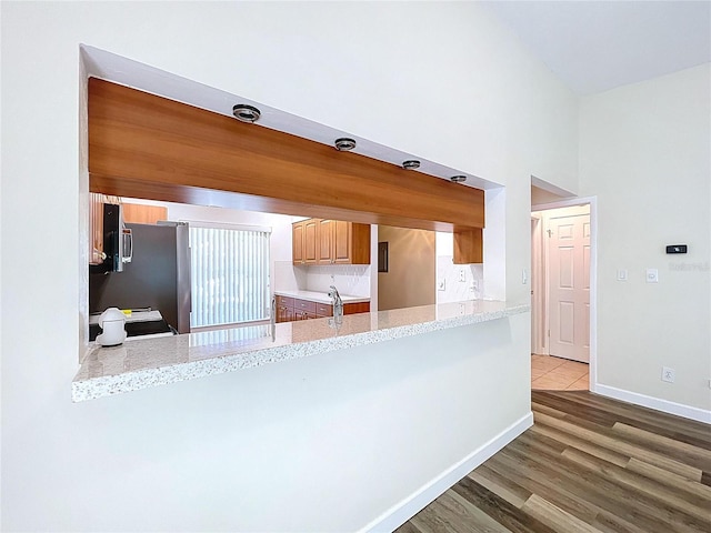 kitchen featuring baseboards, a peninsula, a towering ceiling, wood finished floors, and light stone countertops