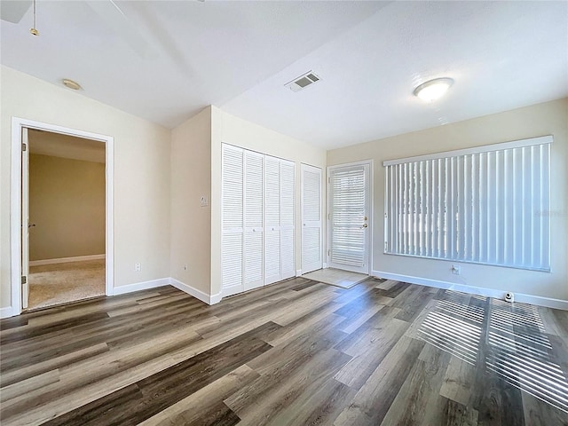 unfurnished bedroom with a closet, visible vents, baseboards, and wood finished floors