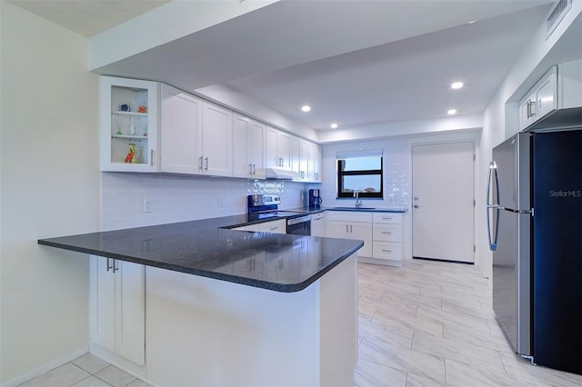 kitchen with appliances with stainless steel finishes, white cabinets, backsplash, a sink, and a peninsula