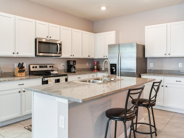kitchen with a sink, light tile patterned floors, stainless steel appliances, a kitchen bar, and white cabinetry