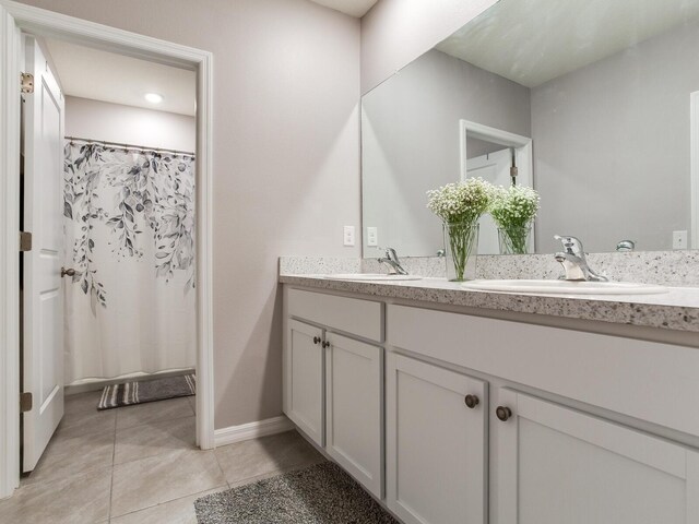bathroom with baseboards, tile patterned flooring, a sink, and double vanity