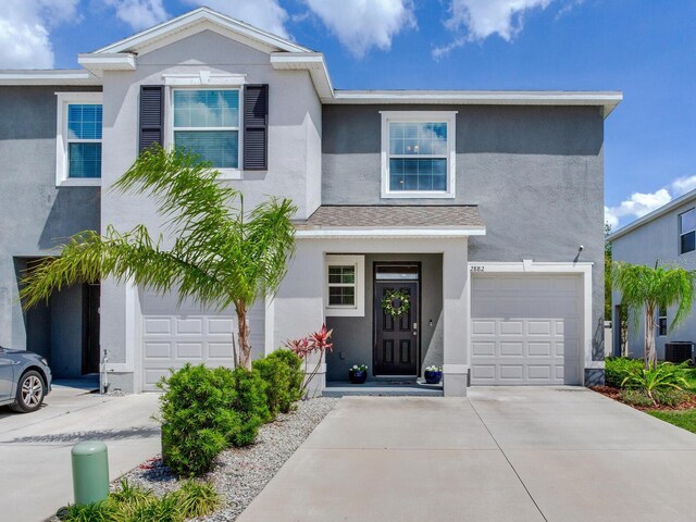 traditional home featuring stucco siding, driveway, central AC, and a garage