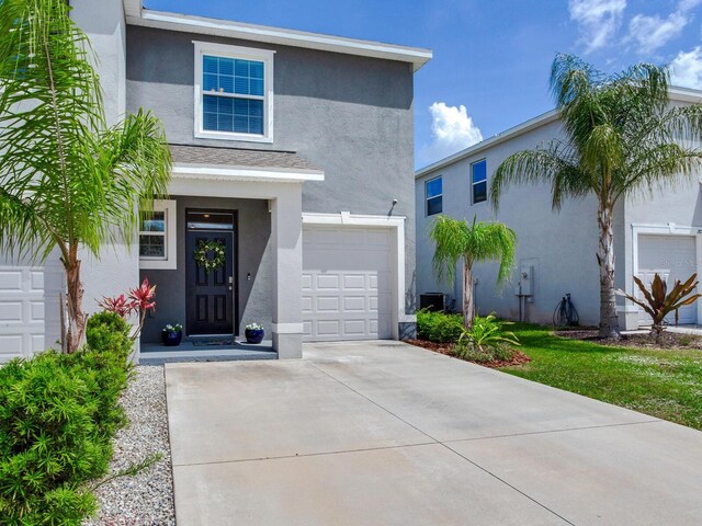 view of front of house with a garage, concrete driveway, central AC, and stucco siding
