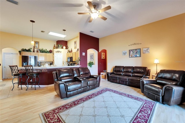living room with arched walkways, light wood-type flooring, and ceiling fan