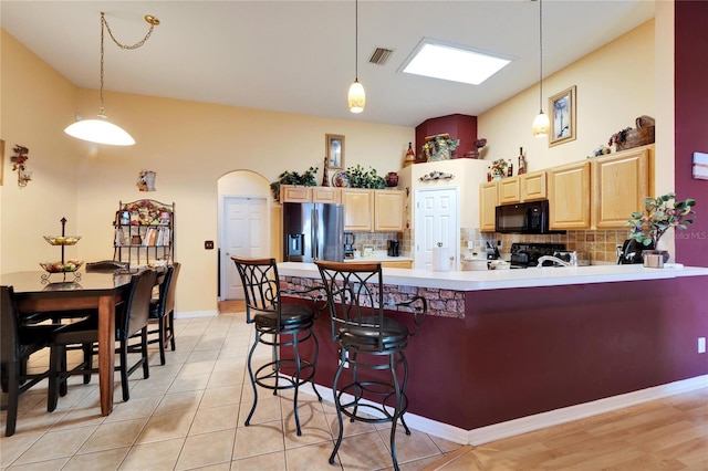 kitchen featuring stainless steel fridge, black microwave, light brown cabinetry, tasteful backsplash, and a peninsula