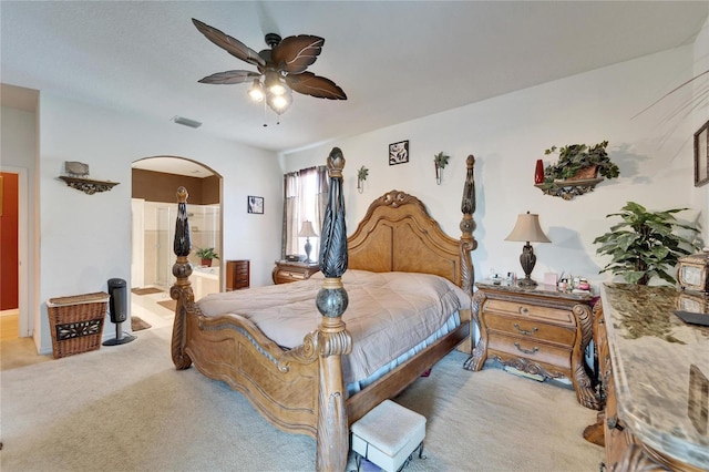 bedroom with light colored carpet, arched walkways, ensuite bathroom, and ceiling fan
