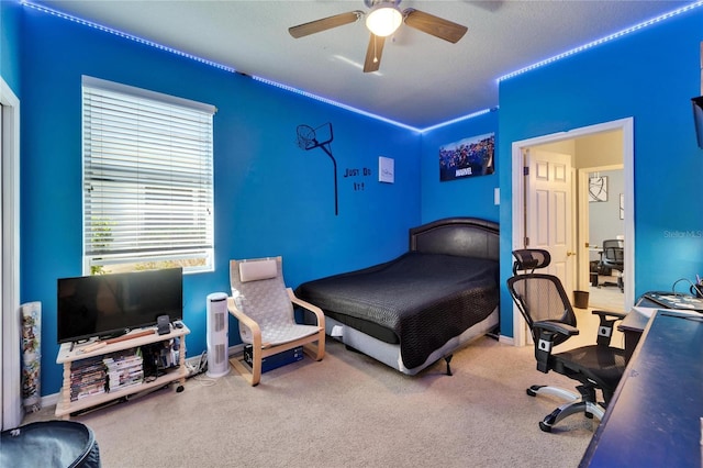 carpeted bedroom with an office area, ceiling fan, and baseboards