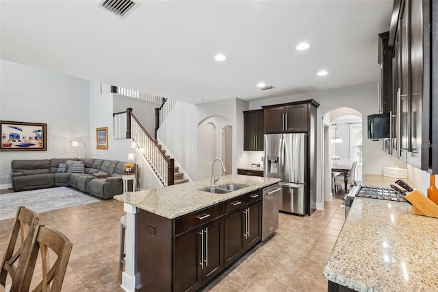 kitchen with dark brown cabinetry, visible vents, stainless steel appliances, arched walkways, and a sink