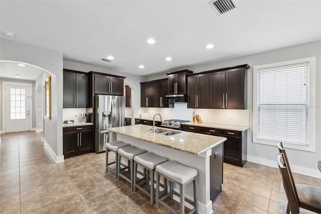 kitchen with stainless steel refrigerator with ice dispenser, visible vents, arched walkways, range hood, and a sink