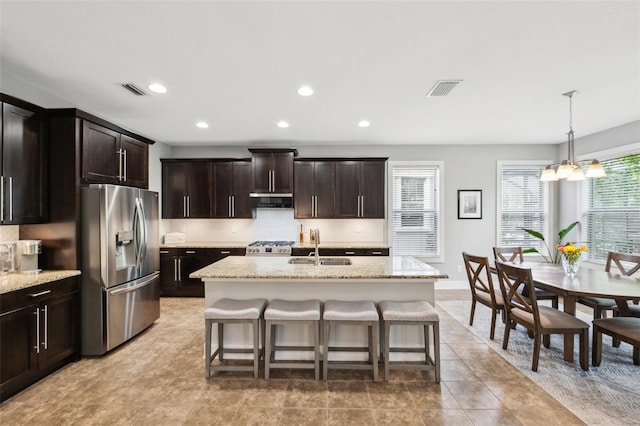 kitchen with tasteful backsplash, an inviting chandelier, stainless steel fridge, visible vents, and a sink