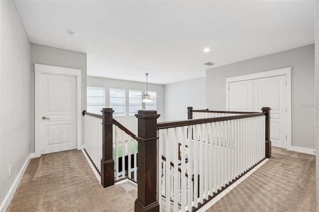 hall with visible vents, baseboards, an upstairs landing, and carpet floors